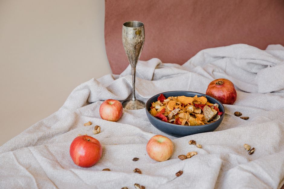 A rustic still life featuring apples, pomegranates, and a silver goblet on a textured clot