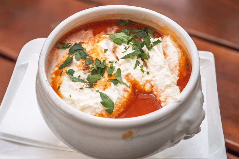 Delicious tomato soup garnished with cream and fresh herbs served in a white bowl.