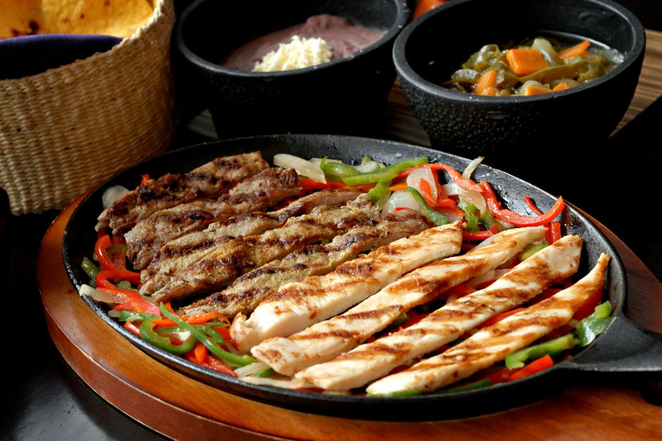 Sizzling platter of chicken and beef fajitas with colorful peppers served with Mexican sid