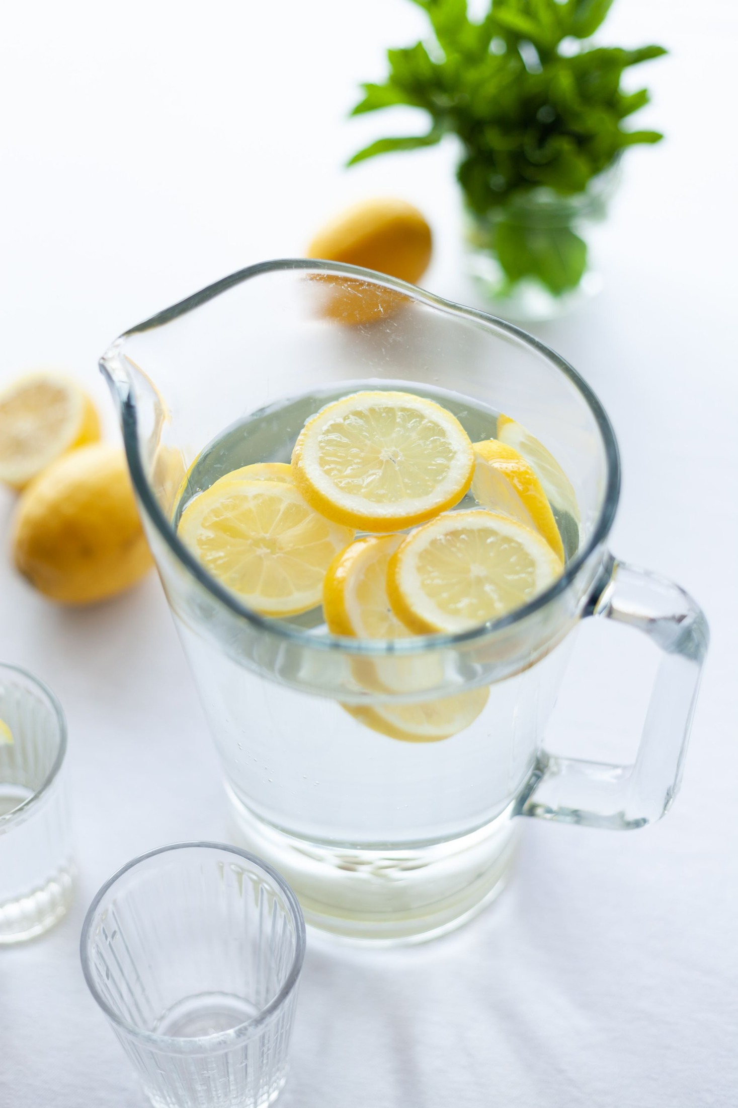 Pitcher of lemon water beside lemons and mint on a light table.