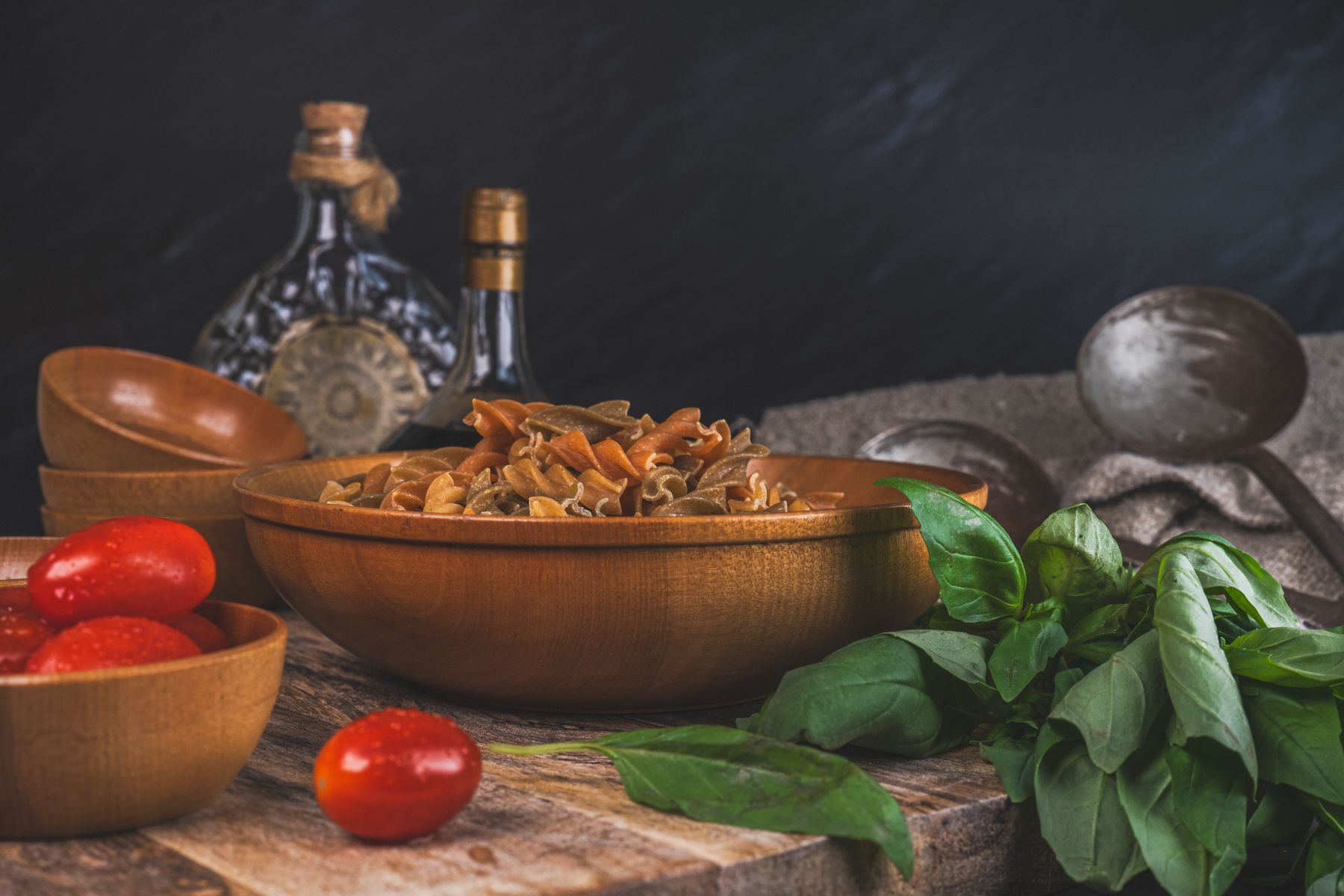 Uncooked whole-wheat pasta with tomatoes and basil in a kitchen ingredient arrangement.