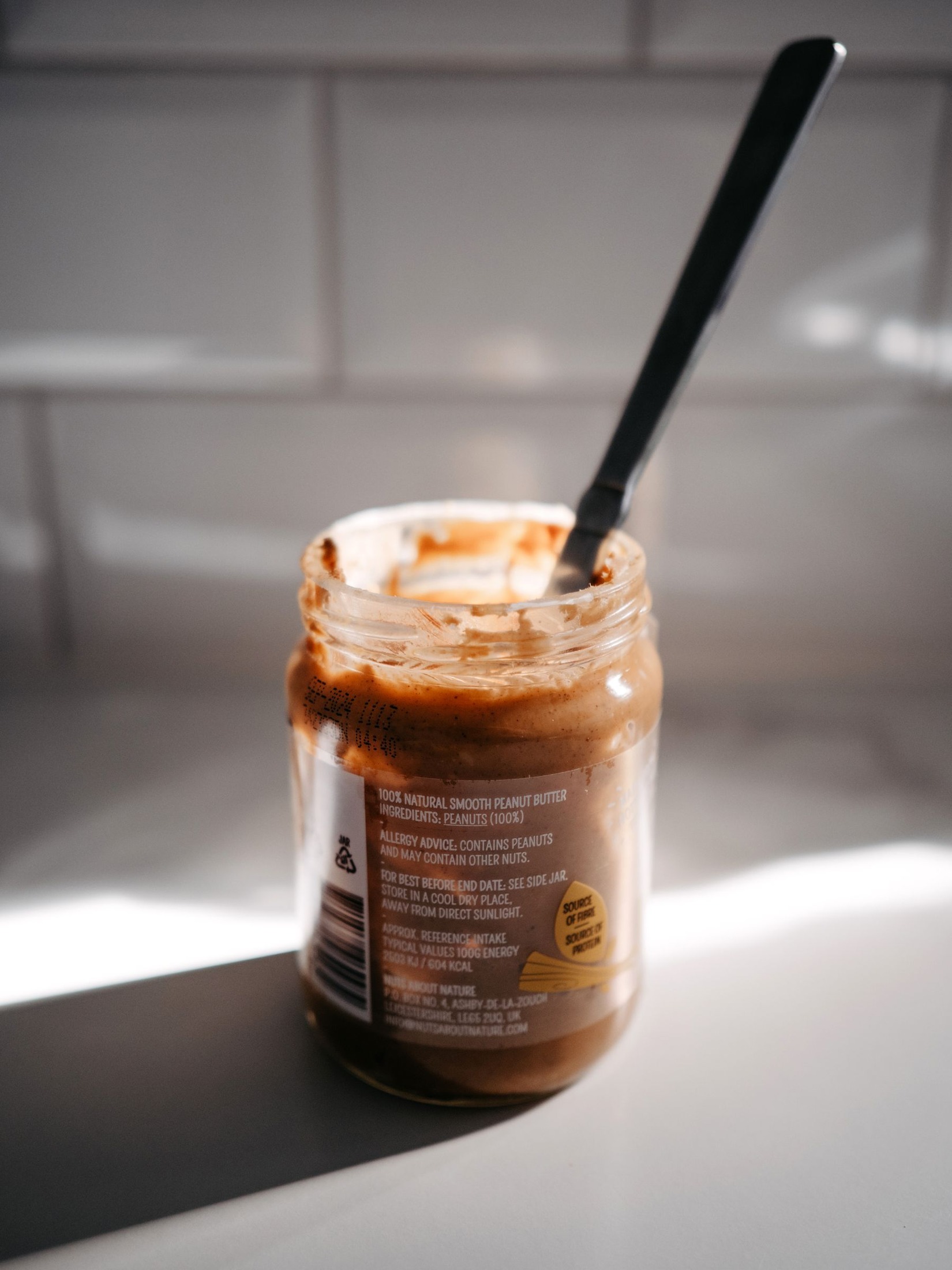 Jar of peanut butter and knife in a sunlit kitchen.