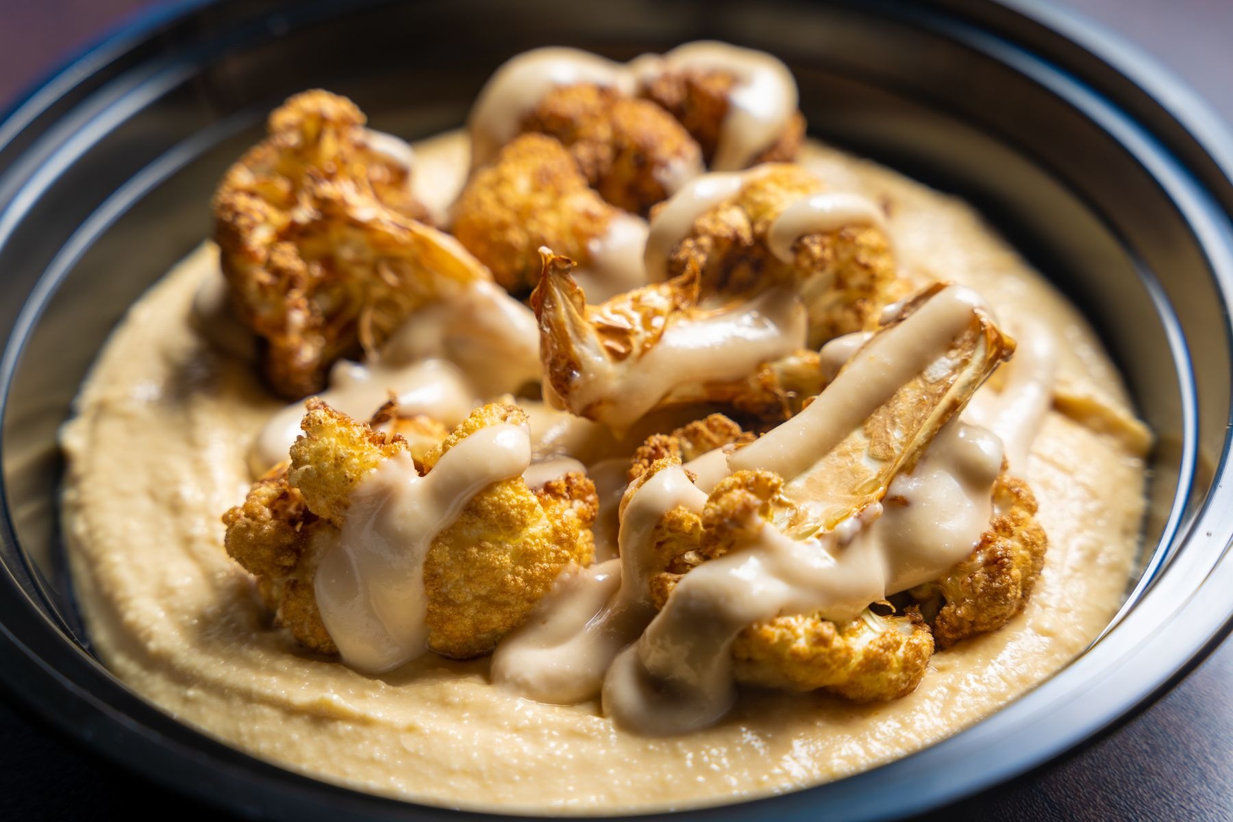 Roasted cauliflower florets in creamy tahini-like sauce in a dark bowl.
