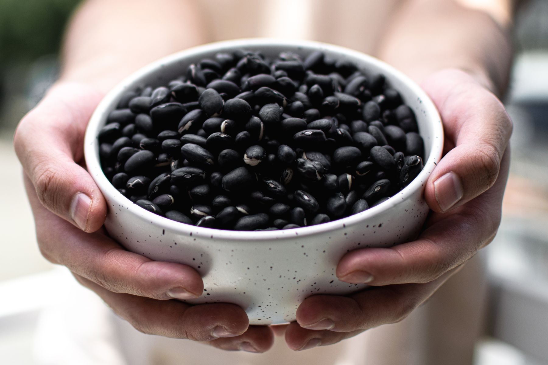 Hands holding a bowl of black beans.