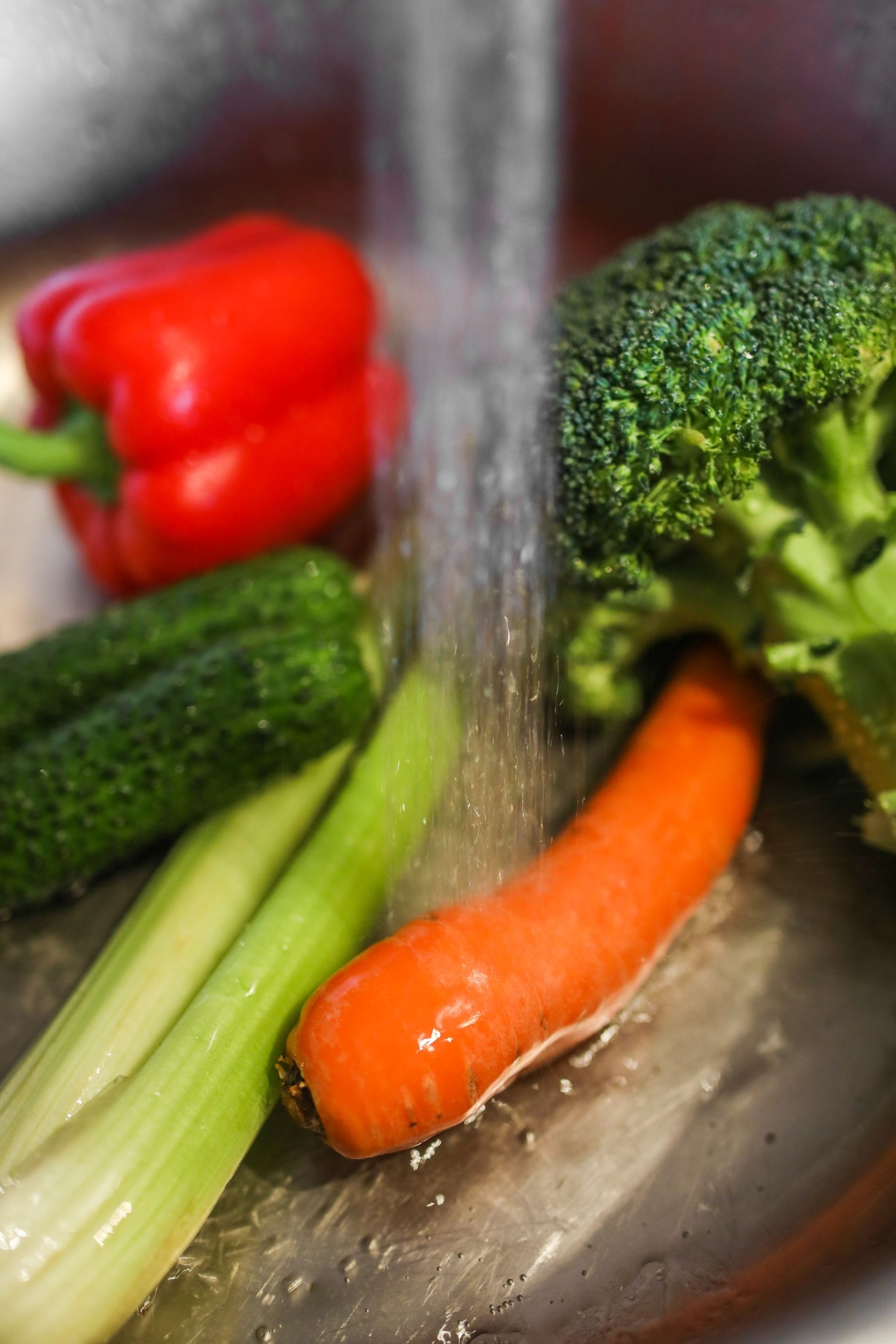 Broccoli, pepper, celery, cucumber and carrot rinsed in a metal bowl.