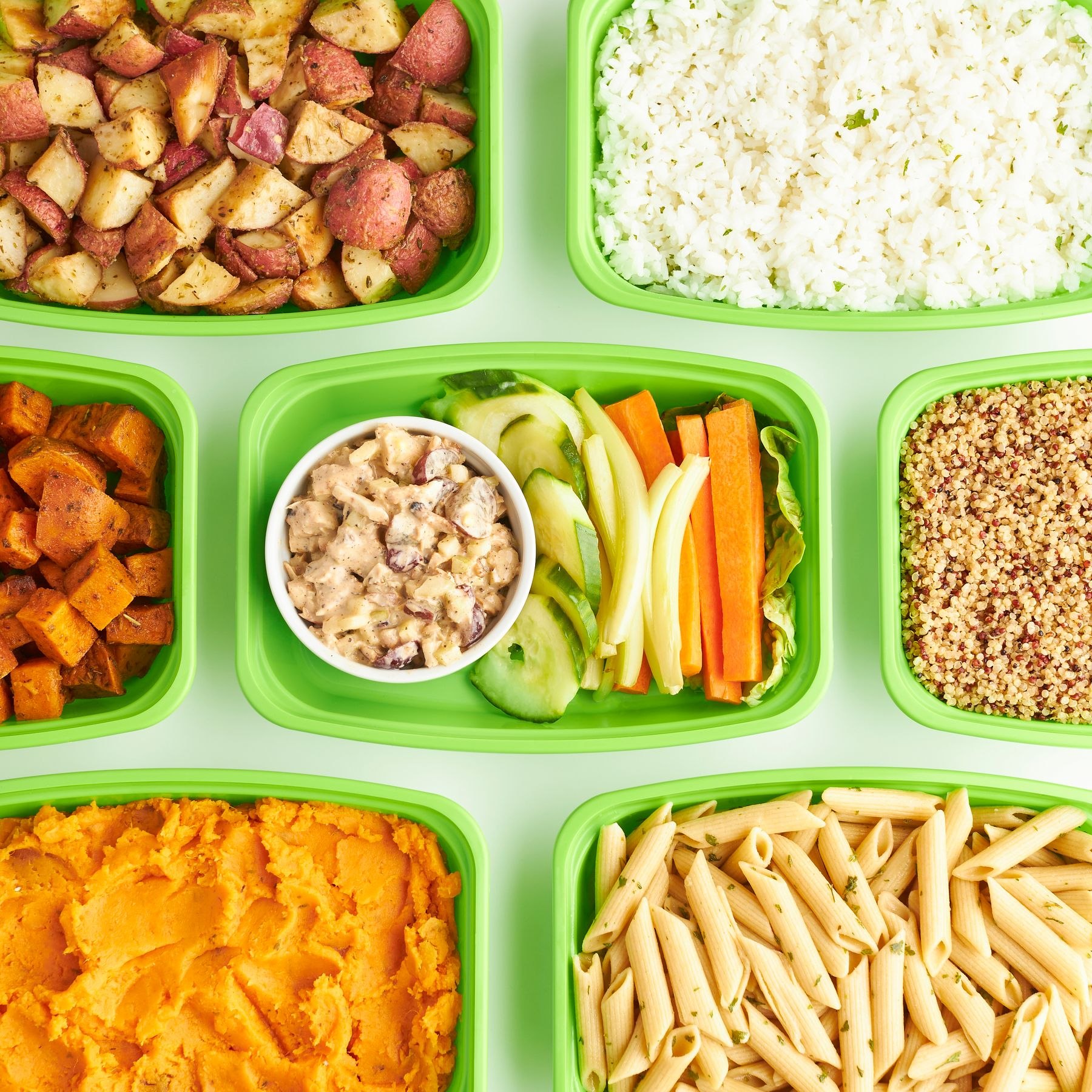 Prepared pasta, vegetables and grains divided into green containers.