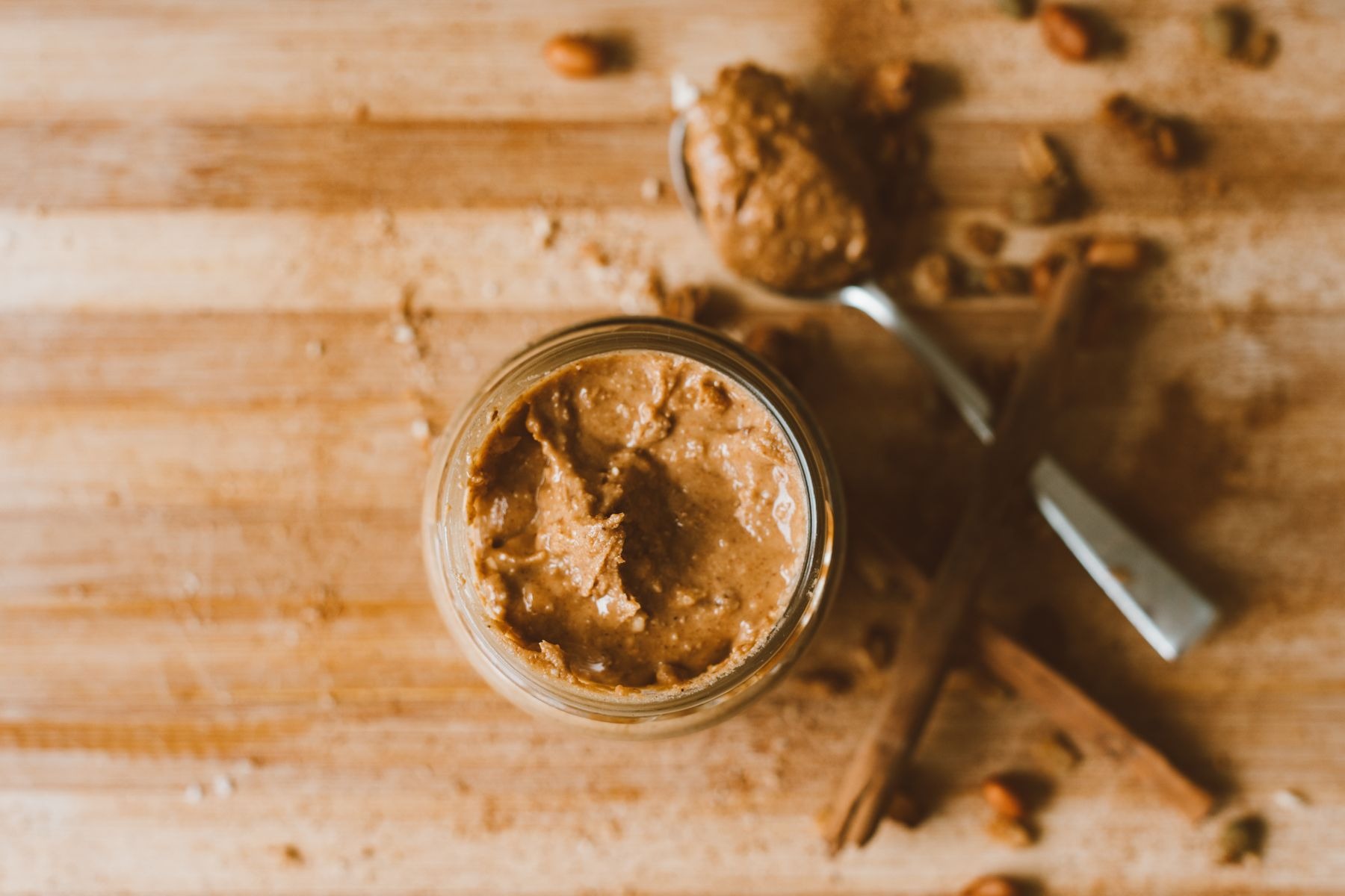 Peanut butter in a glass jar with spoon on a wooden surface.
