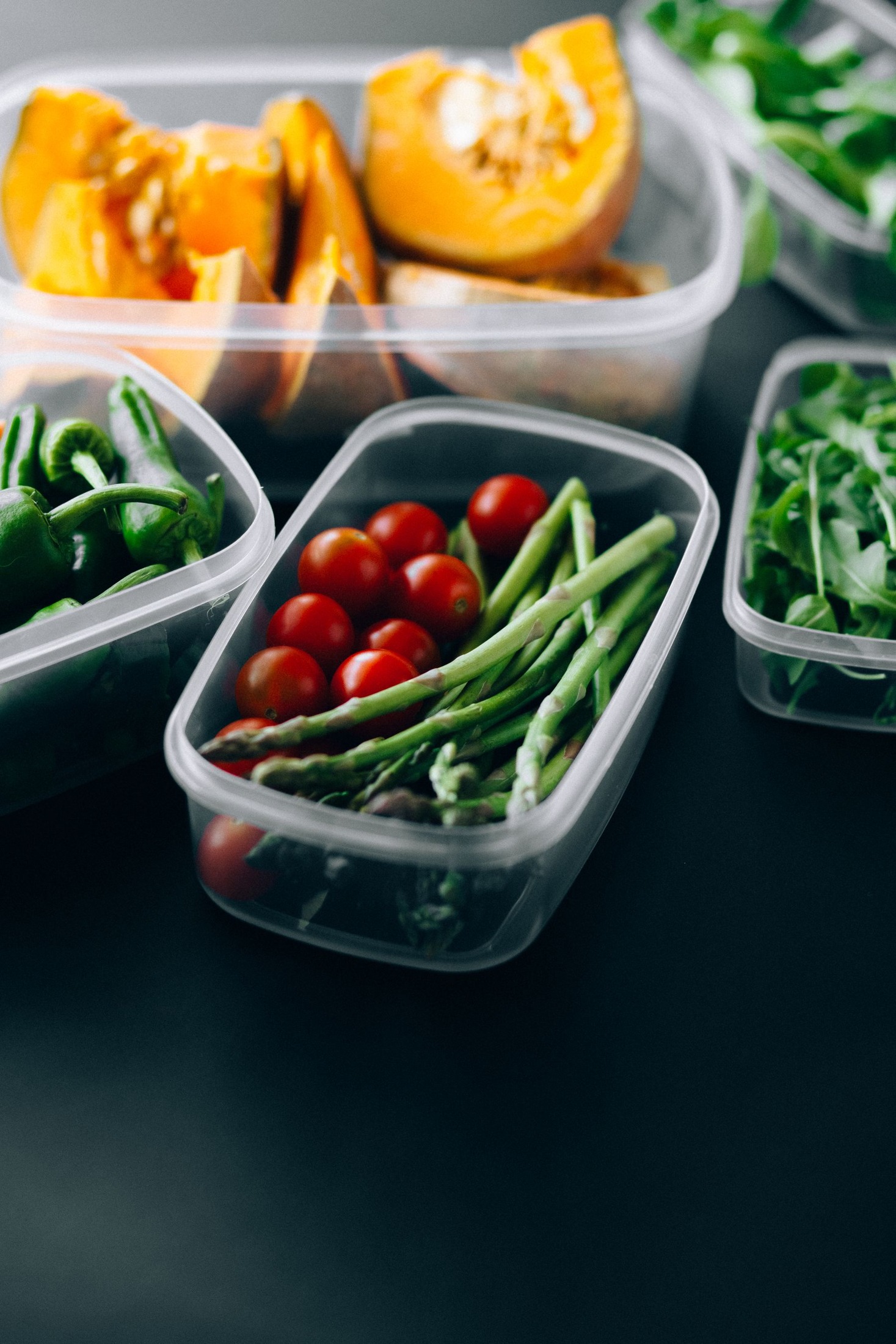 Fresh vegetables arranged in plastic storage containers.