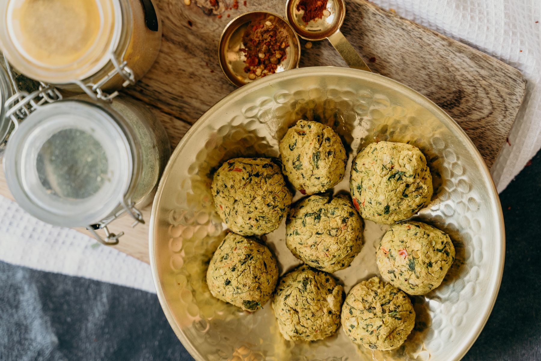Overhead falafel on a bronze plate with herbs and kitchen props.