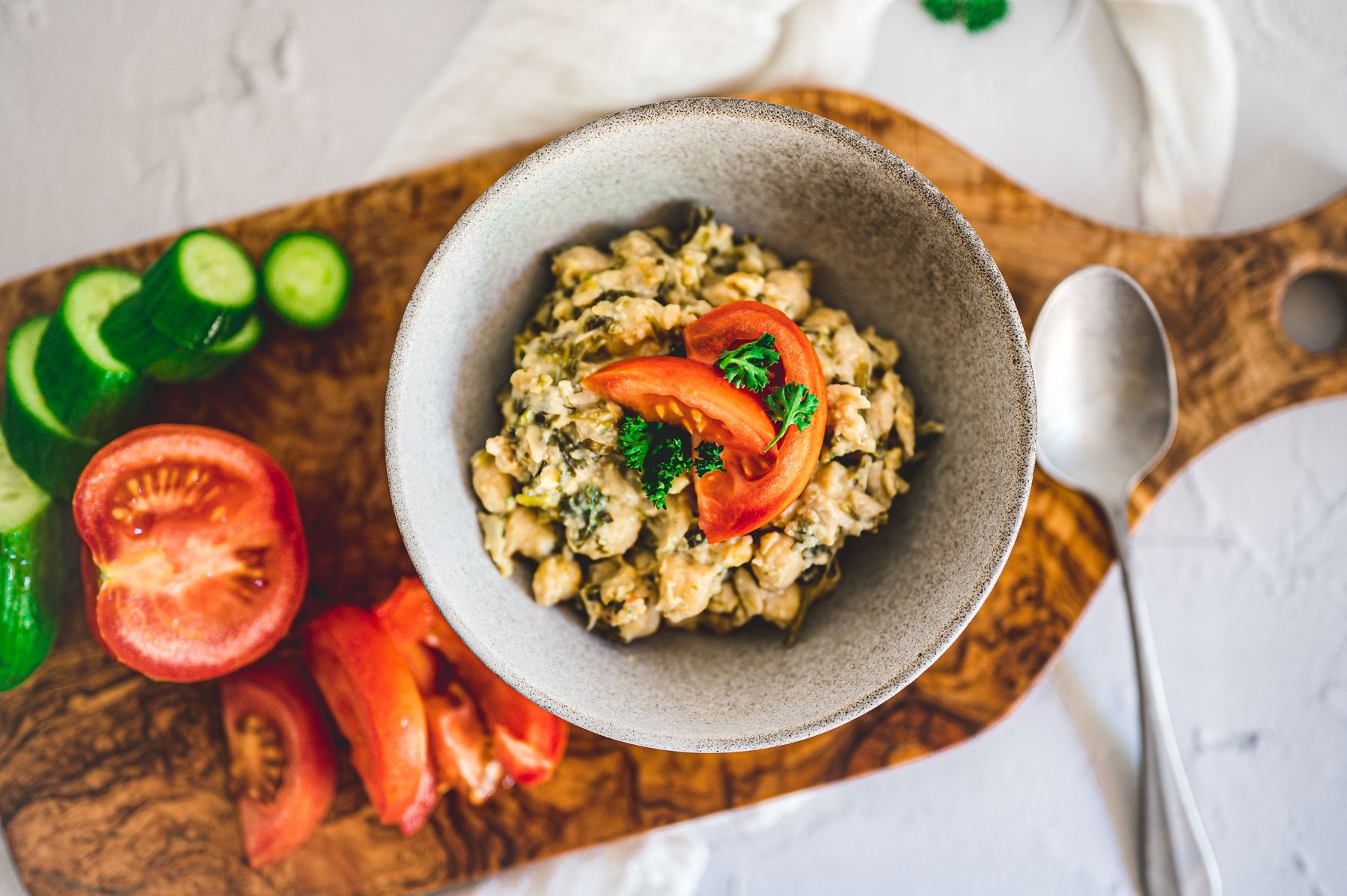 Cooked pulses with chopped greens and tomato garnish; sliced tomato and cucumber alongside the bowl.