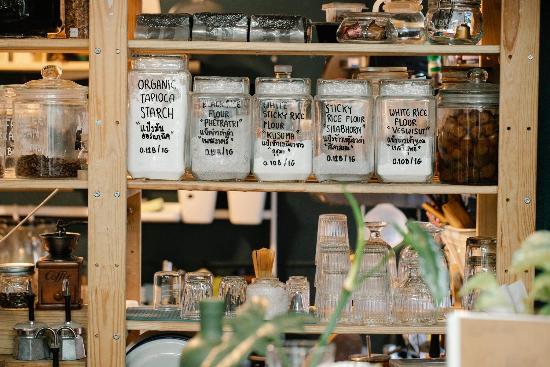Dry food and flour jars with glassware on wooden pantry shelves.