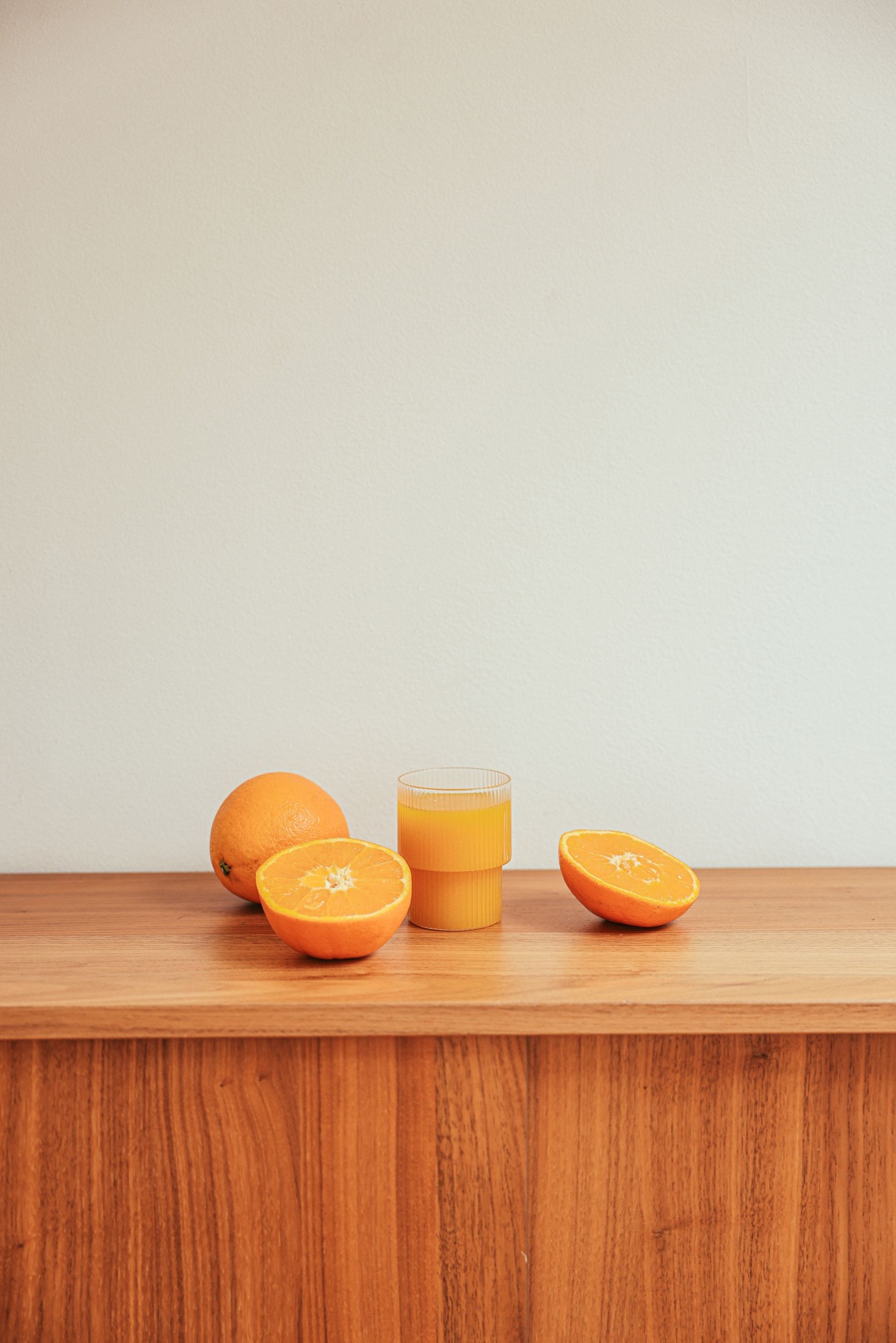 Orange halves and segments on a wooden work surface against a pale wall.
