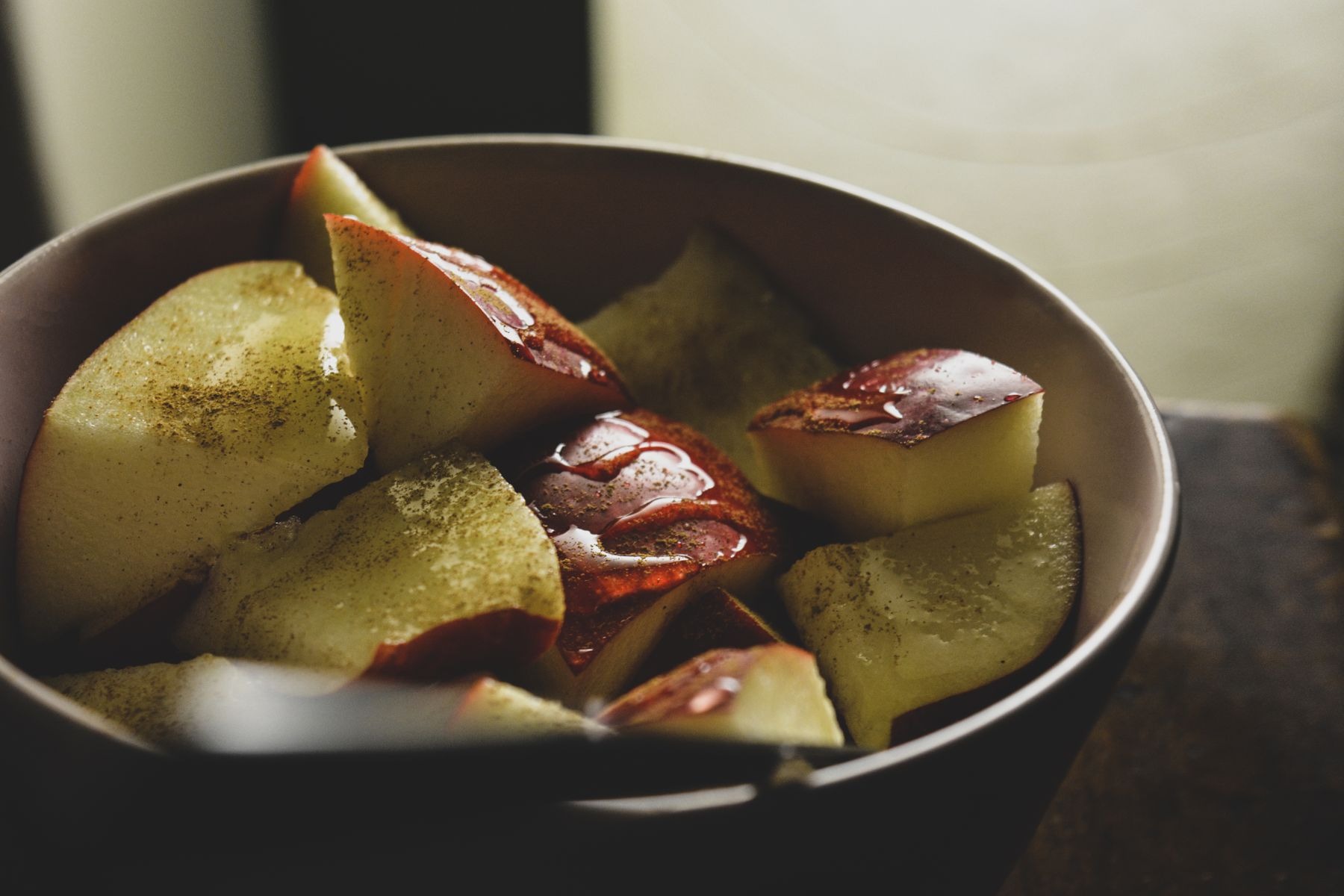 Sliced apples in a bowl sprinkled with cinnamon.