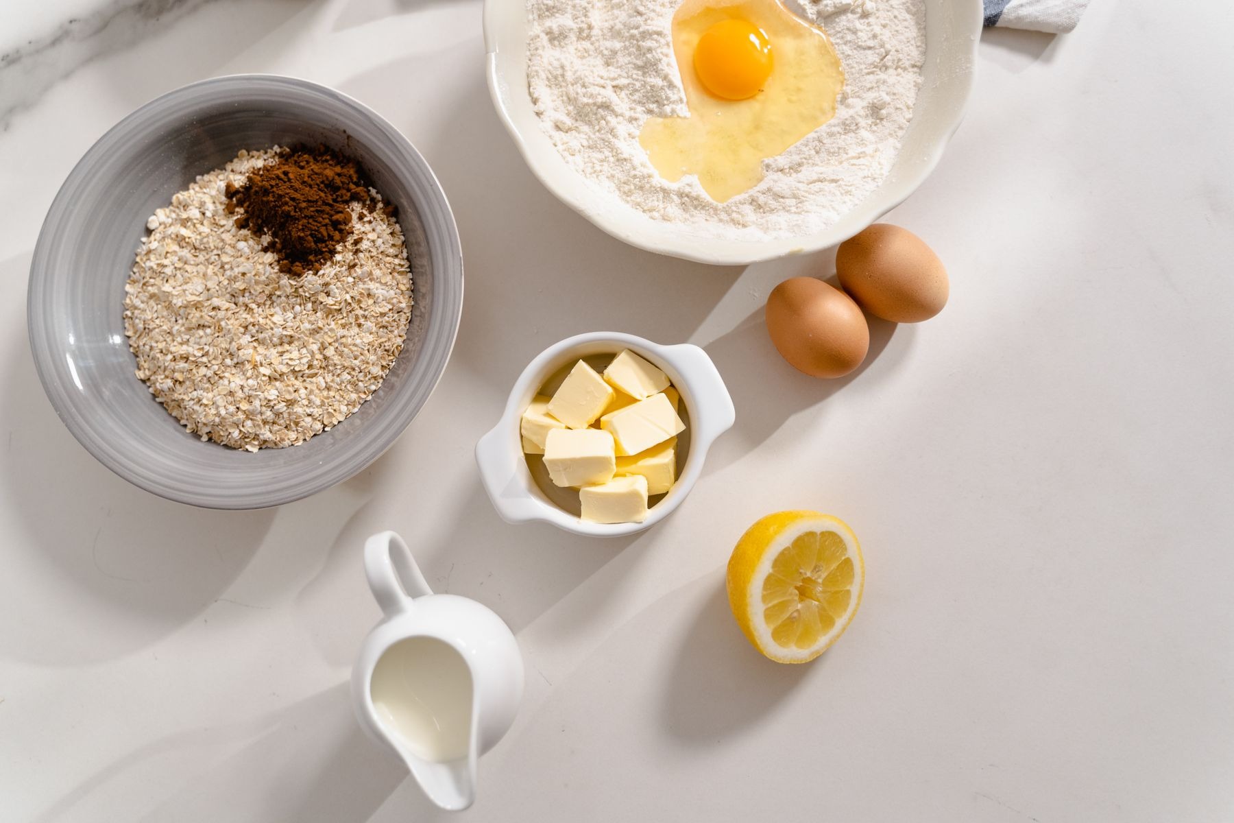 Flour, eggs, lemon and other baking ingredients on a white surface.