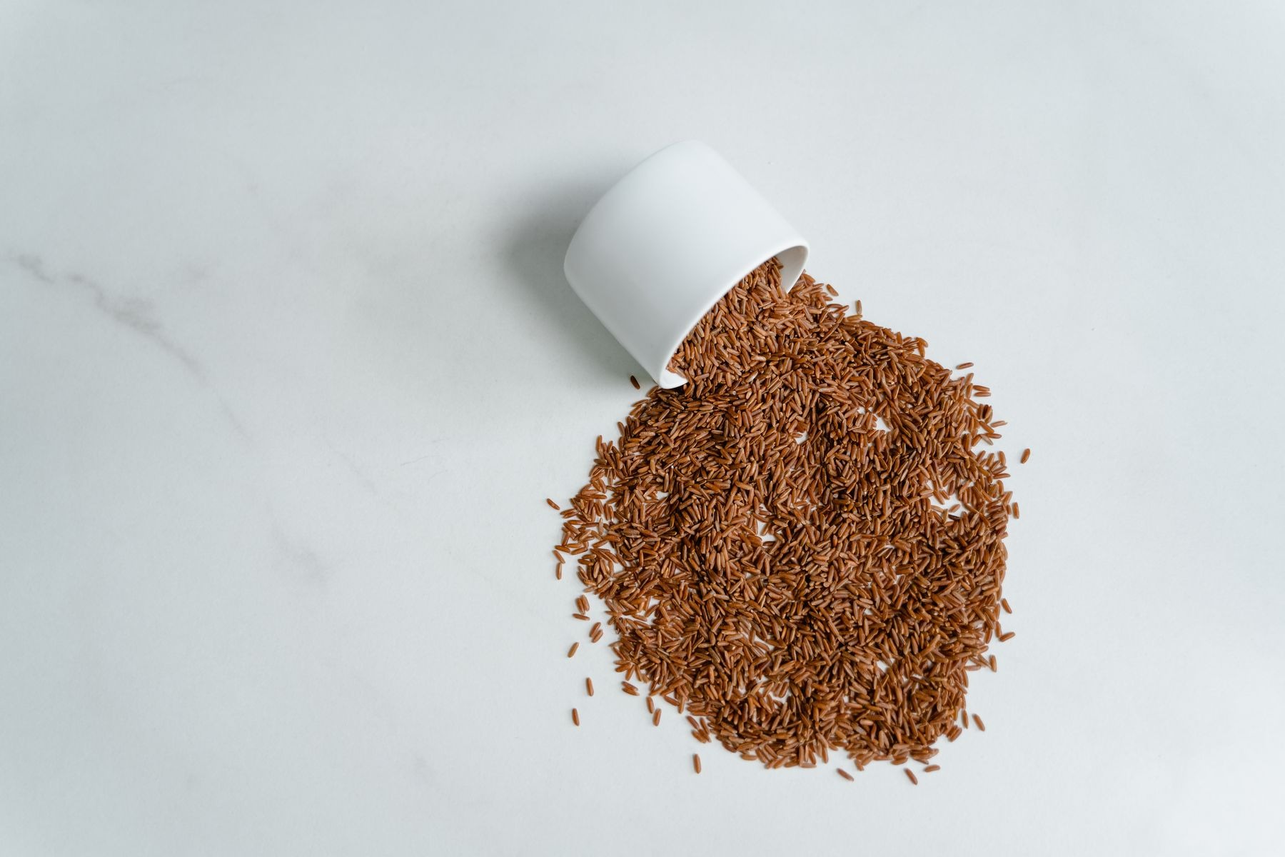 Dry brown rice spilling from a white cup onto a counter.
