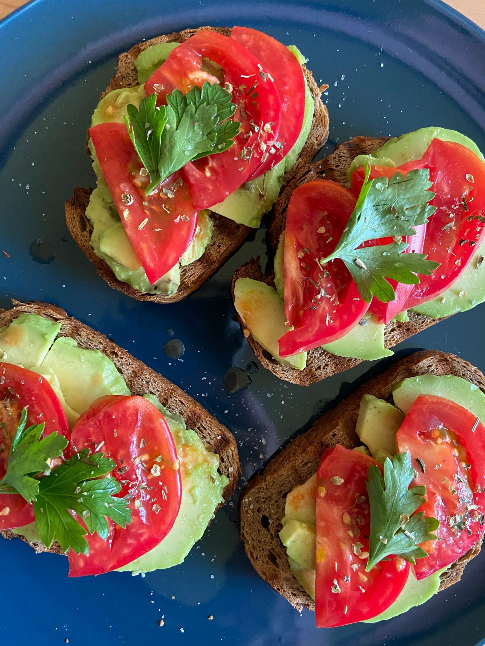 Sliced avocado and tomato toast on a blue plate.